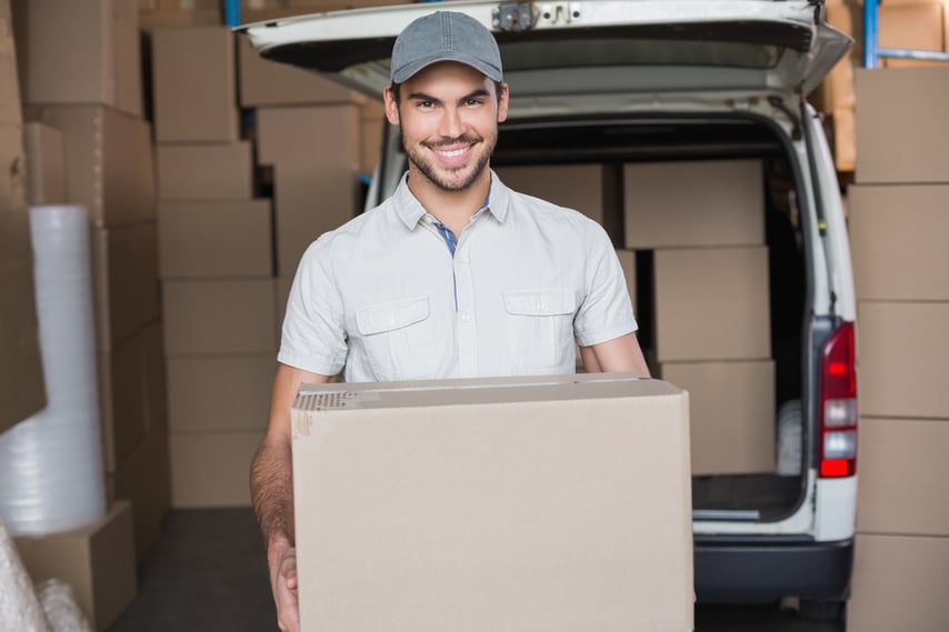 Delivery driver smiling at camera holding box in a large warehouse